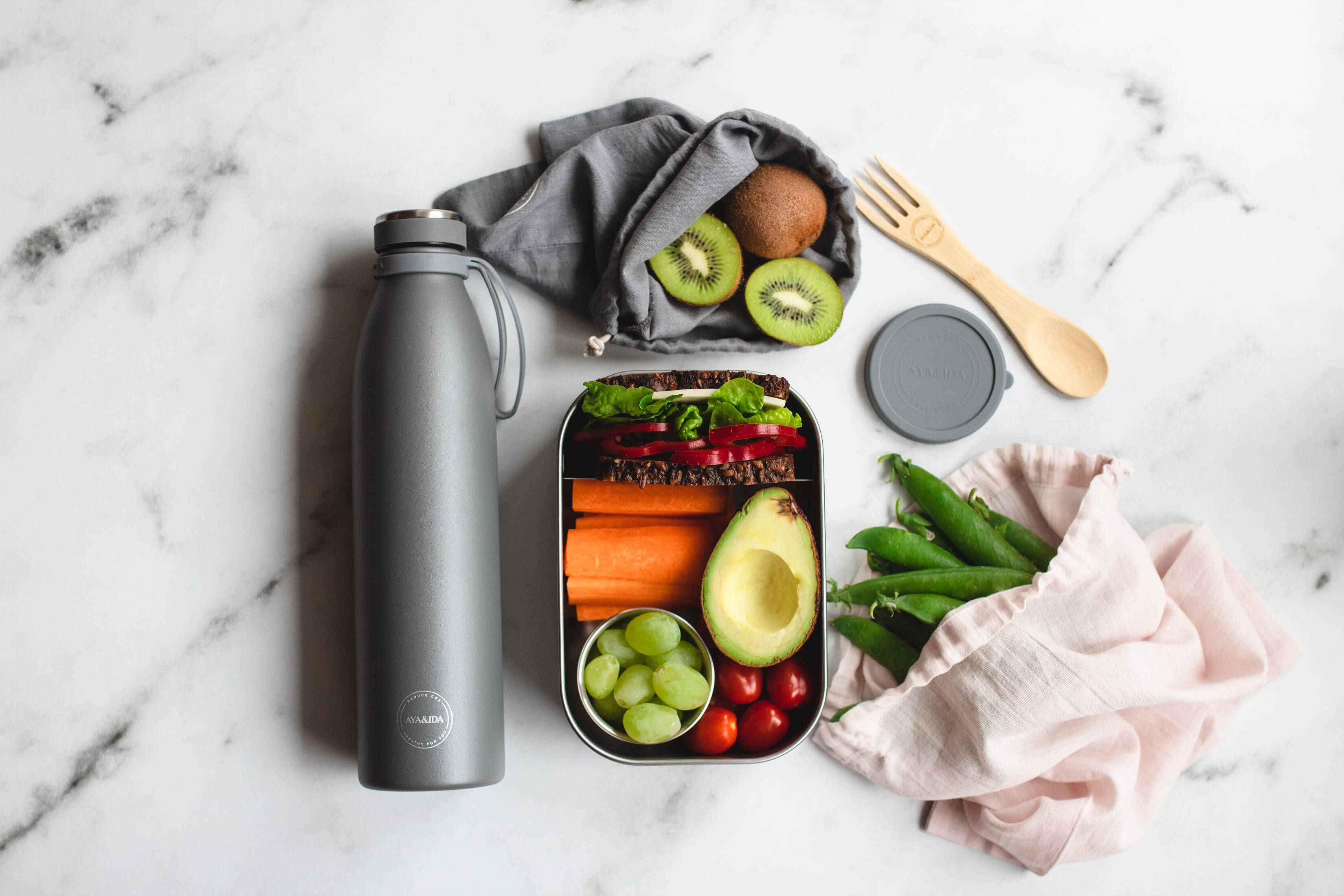 Her ses en baggrund af en marmor bordplade, hvorpå der ligger en åben madkasse fyldt med sund mad. 