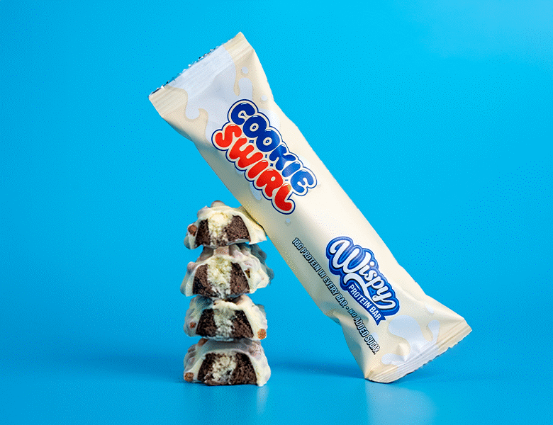 Hvid proteinbar fra Wispy står indpakket op ad udpakkede proteinbarer. Det er på en meget lyseblå baggrund