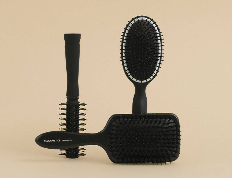 Her ses tre sorte M.Cosmetics hårbørster på en beige baggrund. 