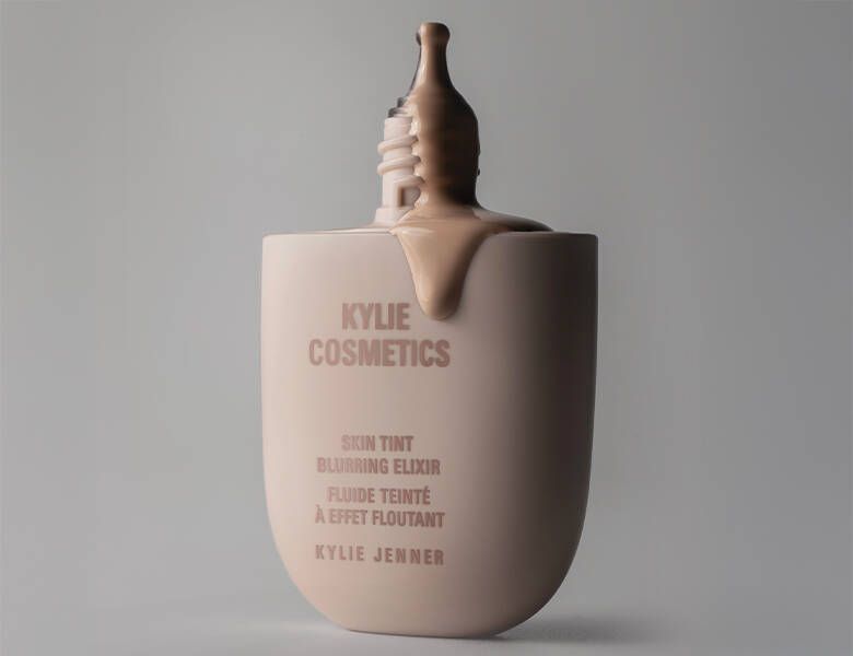 Her ses en grå baggrund med et Kylie Cosmetics produkt i midten. Produktet er åbent og noget af skin tinten kommer ud. 