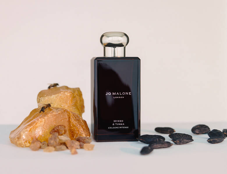 Her ses en beige baggrund med en sort Jo Malone London cologne. I siderne er der sten og rav.