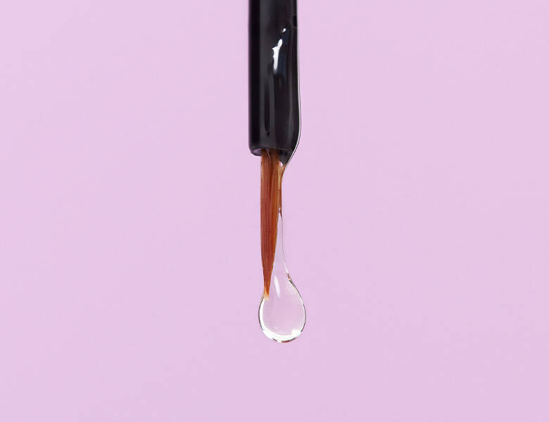 Her ses en lyserød baggrund med en dråbe serum for enden af en pensel.