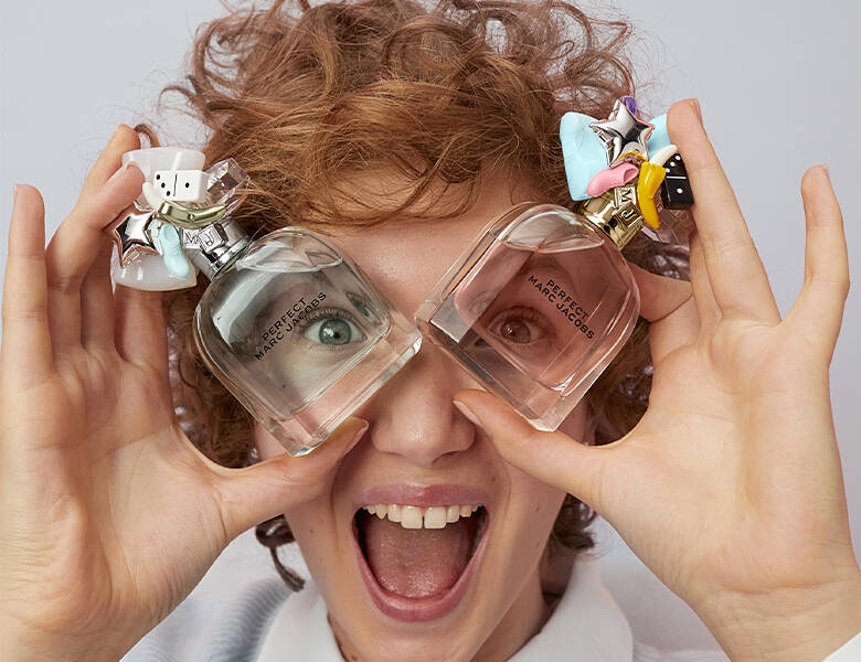 Her ses ansigtet af en kvinde med åben mund. Hun holder en parfume op foran hvert øje.