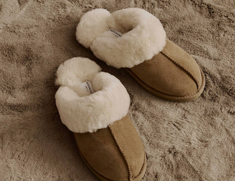 Her ses et par brune og hvide hjemmesko stående på et blødt brunt tæppe.