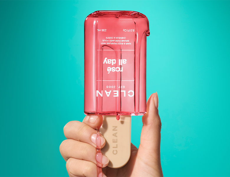 Her ses et billede af et CLEAN-produkt formet som en ispind holdt i en hånd mod en turkis baggrund. På produktet står teksten “CLEAN EST. 2003 rosé all day”.