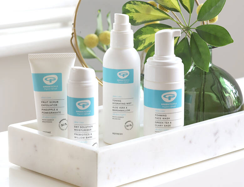 Her ses fire hvide og blå Green People produkter på en hvis marmor bakke med en grøn plante og et guldspejl.