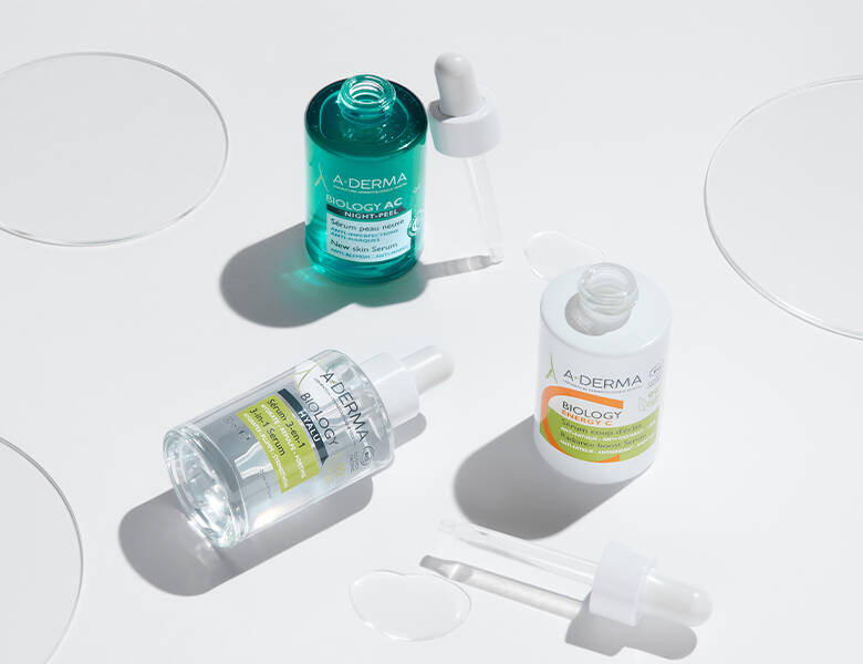 Her ses tre forskellige A-DERMA produkter liggende/stående på et hvidt bord. 