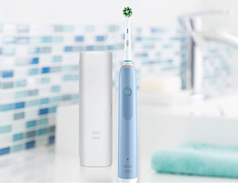 Her ses en lyseblå elektrisk tandbørste samt en hvid beholder. Baggrunden er et slørret badeværelse.