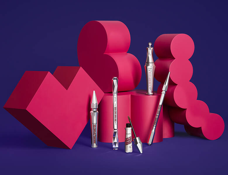 Her ses en mørkelilla baggrund med røde figurer, som fem brynprodukter står op af.