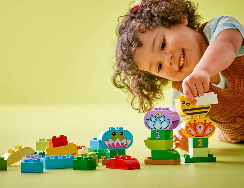 Her ses en grøn baggrund med et barn, som leger med nogle større legoklodser. 