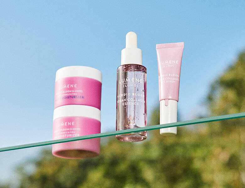 Her ses fire lyserøde Lumene produkter. Baggrunden er nogle grønne træer og en blå skyfri himmel. 