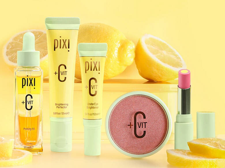 Her ses en gul baggrund med forskellige Pixi Beauty produkter i gule, grønne og lyserøde farver. Der ligger desuden citroner. 