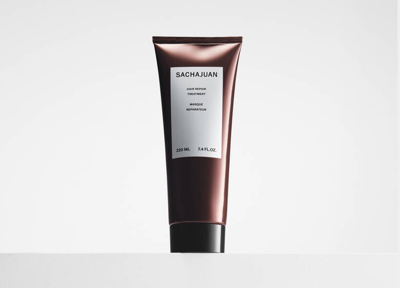 Her ses et billede af et hårprodukt fra SACHAJUAN placeret centralt mod en lys baggrund. På produktet står teksten “SACHAJUAN Hair Repair Treatment”. Produktet er i en mørk, metallisk tube med sort låg.