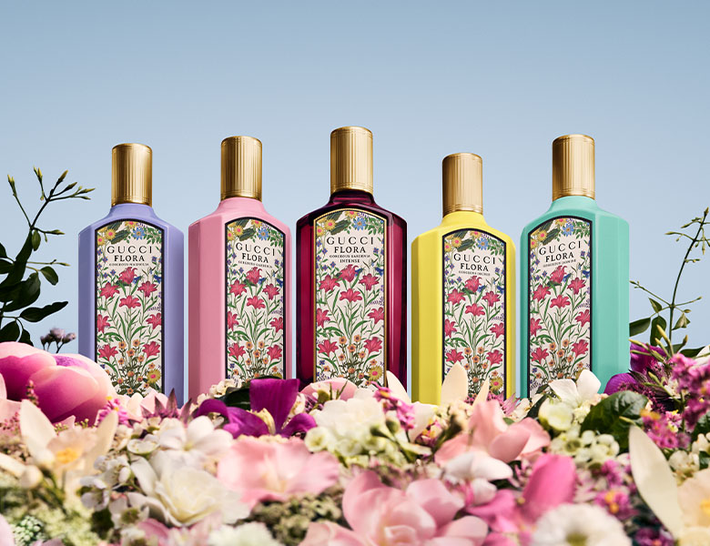 Her ses fem Gucci Flora parfumer stående på nogle blomster og med en lyseblå baggrund.