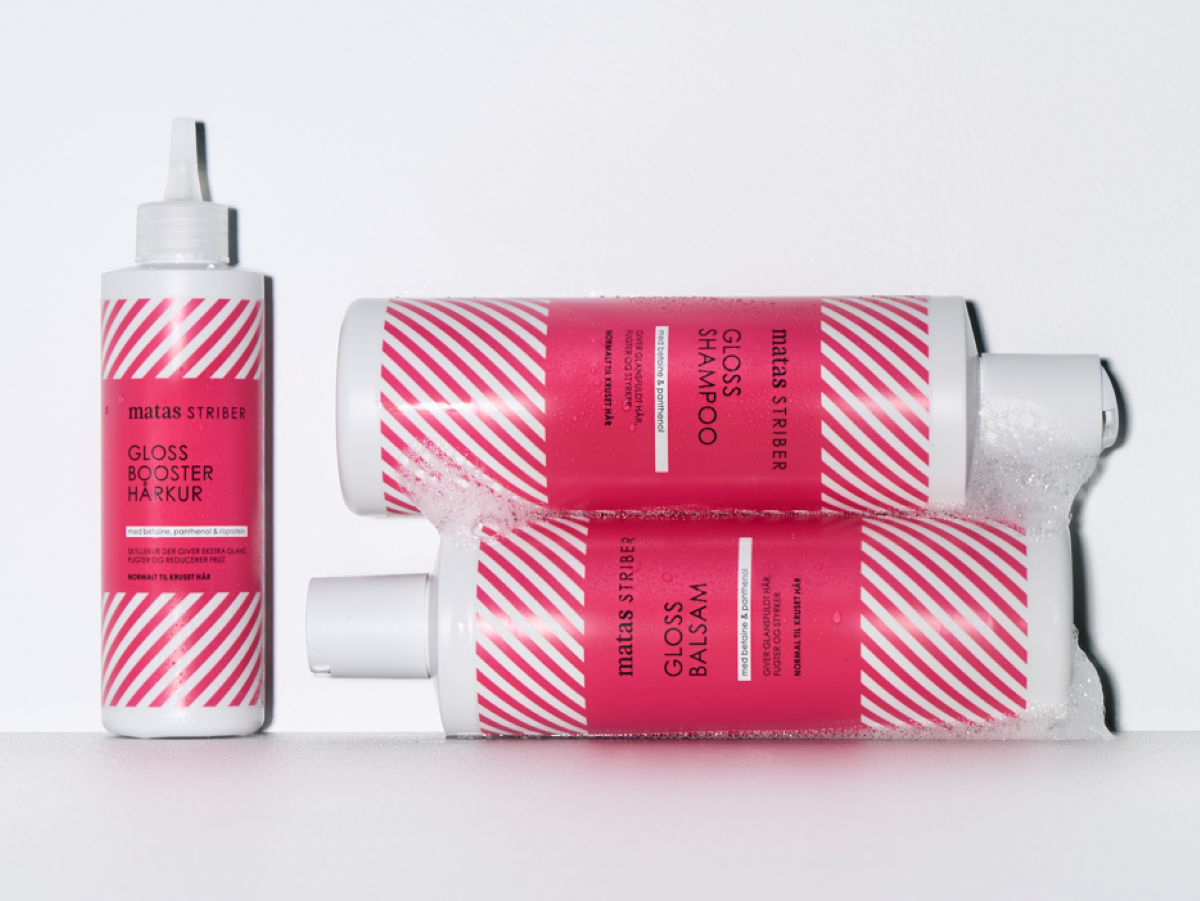 Tre Matas Striber Gloss produkter: En oprejst Gloss Booster Hårkur og to liggende, skummende flasker Gloss Shampoo og Gloss Balsam. Hårkuren indeholder betaine, panthenol & risprotein og giver ekstra glans, fugt samt reducerer frizz. Shampoo og Balsam indeholder betaine & panthenol og giver glansfuldt hår, fugt og styrke. Alle produkterne er til normalt til kruset hår. Hvide flasker med pink diagonale striber.