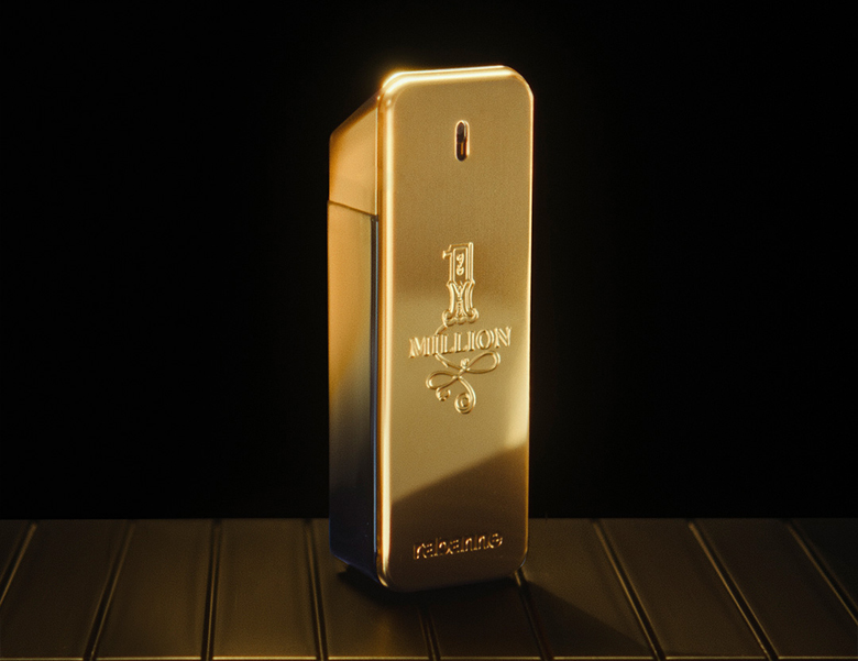 Her ses et billede af en parfumeflakon med teksten “1 MILLION” placeret mod en mørk baggrund. Flakonen er i guldfarvet, rektangulært design med blank overflade.