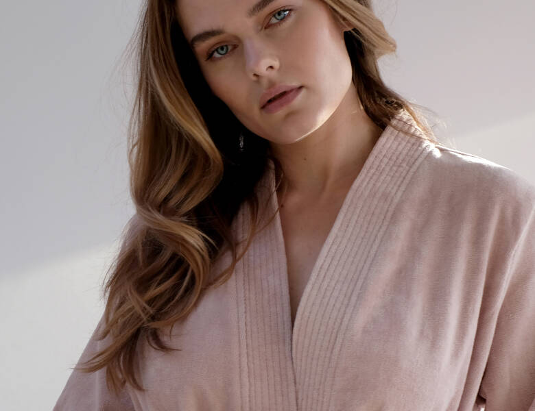 Her ses overkroppen og ansigtet af en kvinde med en lyserød badekåbe på. Baggrunden er lys.