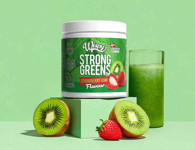 Wispy Nutrition Greens grøn bøtte ovenpå en lysegrøn kasse med lysegrøn baggrund. Der ses en grøn smoothie i baggrunden og en halveret kiwi og et jordbær foran den grønne kasse.