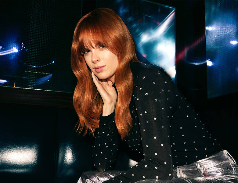 Her ses en mørk baggrund med en kvinde, som har glat rødt hår.