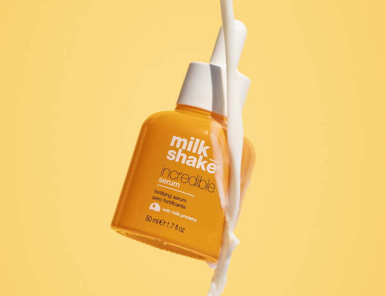Her ses et billede af et produkt fra milk_shake placeret mod en gul baggrund. På flasken står teksten “milk_shake incredible serum”. Produktet er i en orange flaske, og der løber en hvid væske ned langs siden.