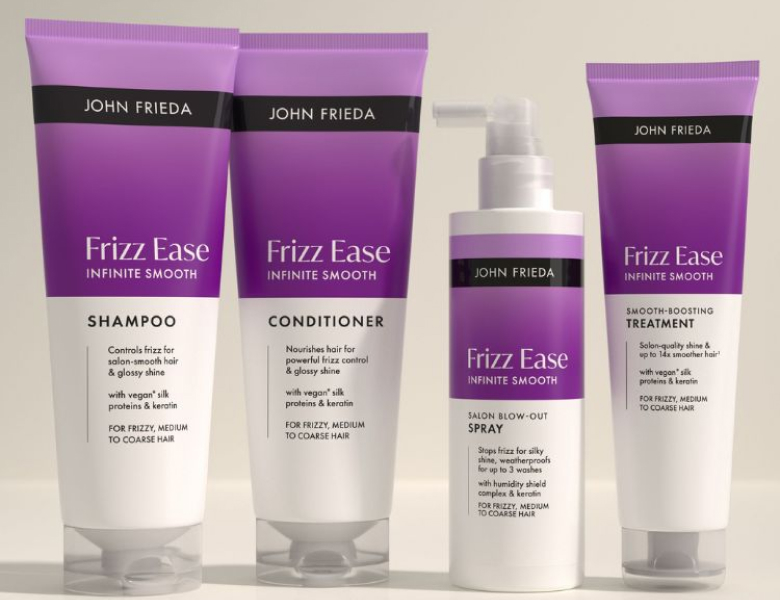 Her ses et billede med hårplejeprodukter fra John Frieda placeret mod en lys baggrund. På produkterne står teksten “Frizz Ease Infinite Smooth”, og serien indeholder blandt andet shampoo, conditioner, spray og treatment. Nederst står teksten “FRIZZ”.