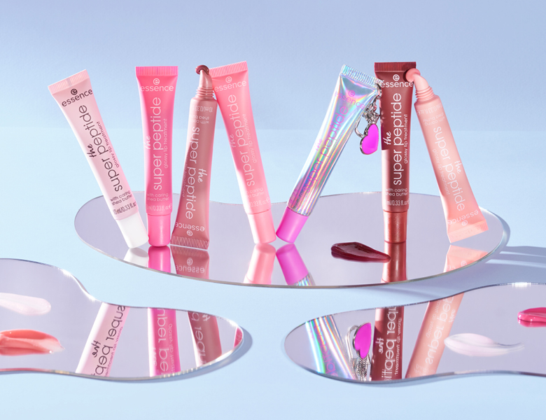 Her ses et billede med flere læbeprodukter fra essence placeret på spejlende overflader mod en lys baggrund. På produkterne står teksten “essence super peptide”. Produkterne er i lyserøde og transparente emballager, og der ses farveprøver omkring dem.