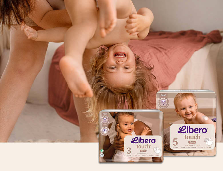 Her ses en mor som holder sit glade barn på hovedet. Ved siden ses to forskellige slags Libero bleer. Baggrunden er et soveværelse.