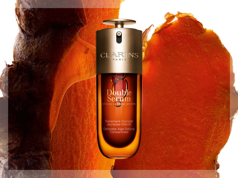 Her ses et brunt Clarins produkt på en rød og brunlig baggrund.