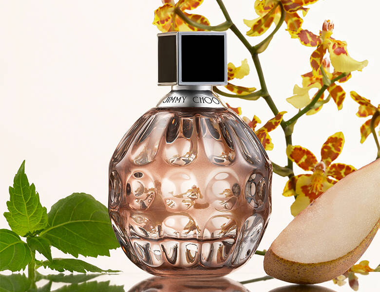 Her ses e hvid baggrund med en pære og nogle grønne planter. Forrest ses en brunlig parfume.