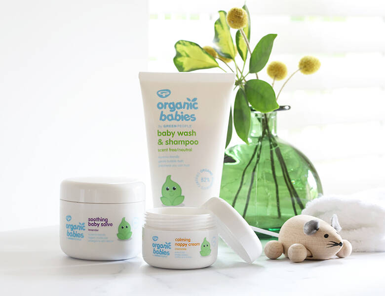 Her ses tre hvide og blå Green People produkter på et hvidt bord med blomster og legetøj på.