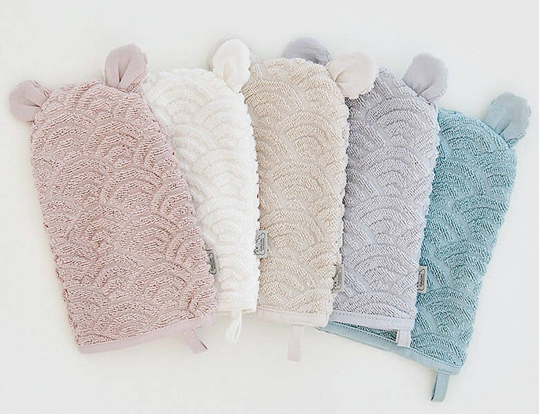 Fem bløde badehandsker i rosa, hvid, beige, lilla og lyseblå ligger side om side på lys baggrund.