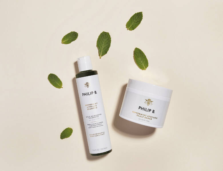 Her ses to hvide Philip B produkter liggende på en lys baggrund med grønne blade omkring sig. 