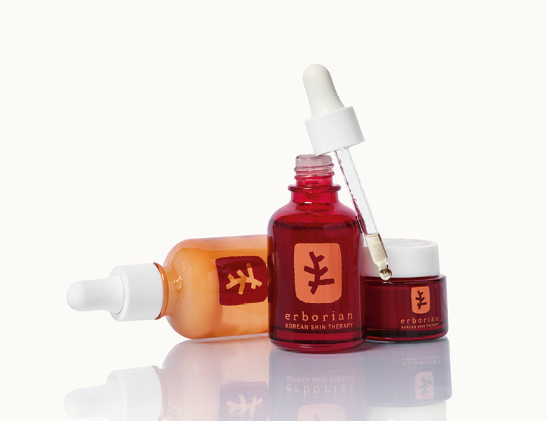 Her ses Erborian hudplejeprodukter – serum og creme i røde og orange flasker på en lys baggrund.
