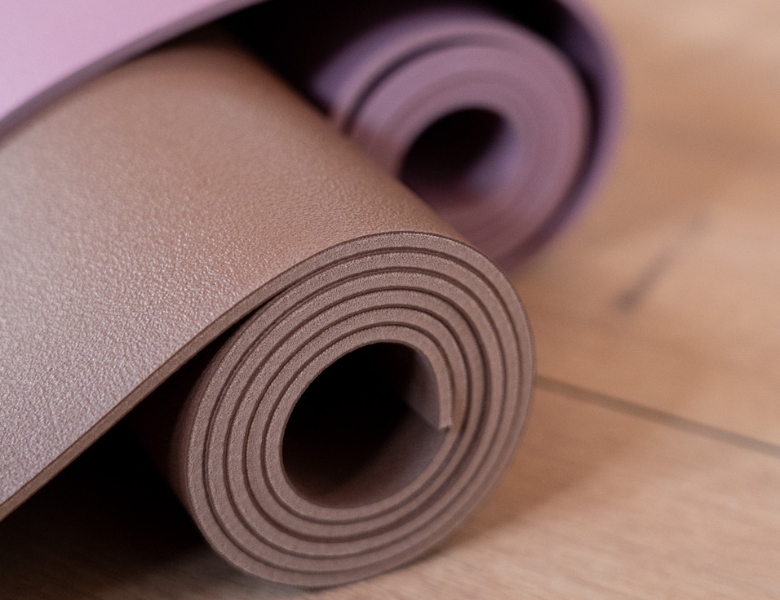 To sammenrullede yogamåtter i brune og lilla nuancer ligger på et trægulv.