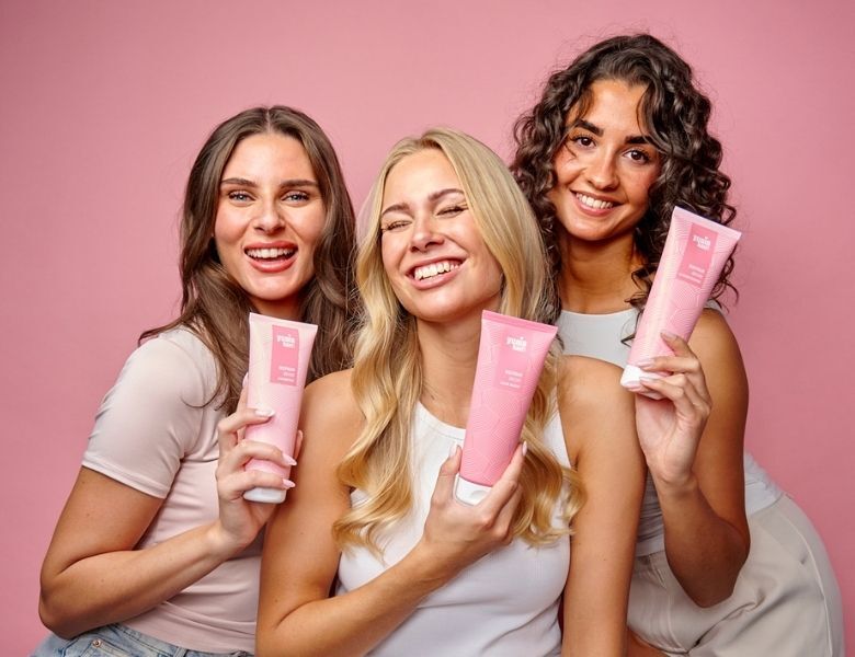Her ses tre kvinder, der holder Yuaia Hair produkter i pink emballage på en lyserød baggrund.