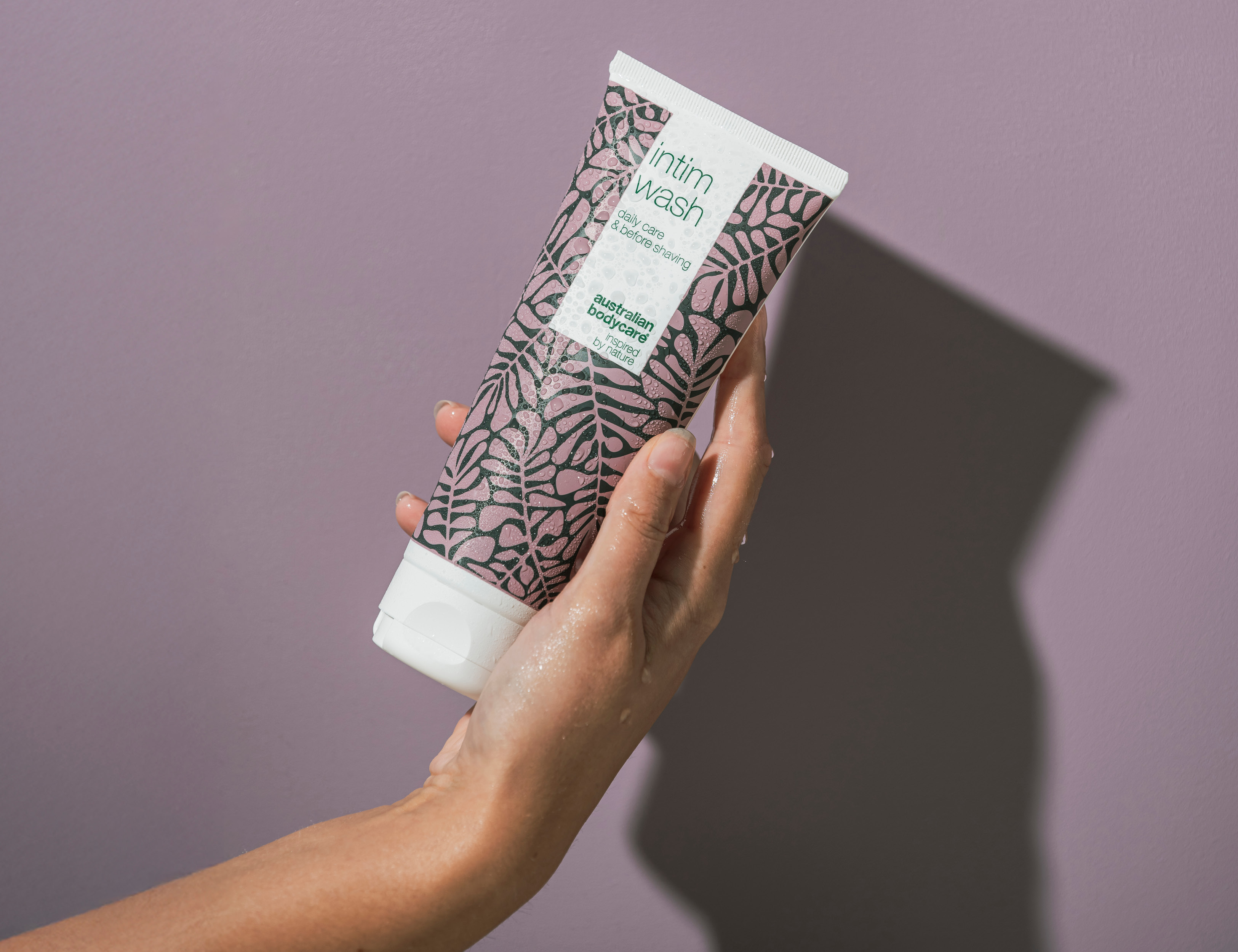 Her ses en hånd, der holder en australian bodycare intim wash på en lilla baggrund.