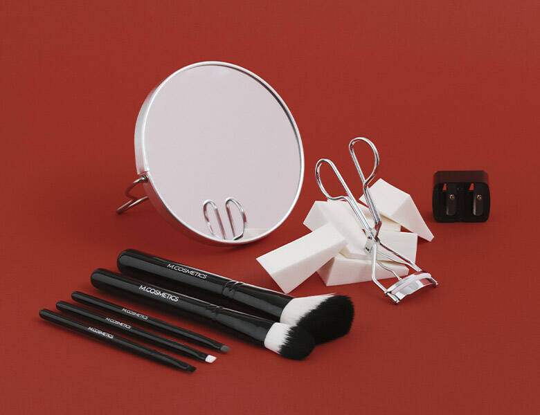 Her ses en rød baggrund med M.Cosmetics produkter på. 