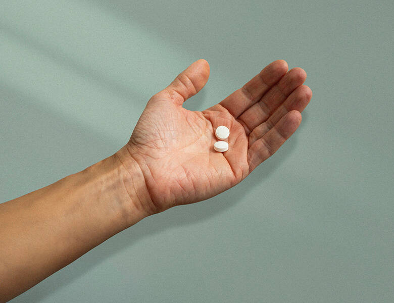 Her ses en hånd med to piller i. Baggrunden er grøn-blå.