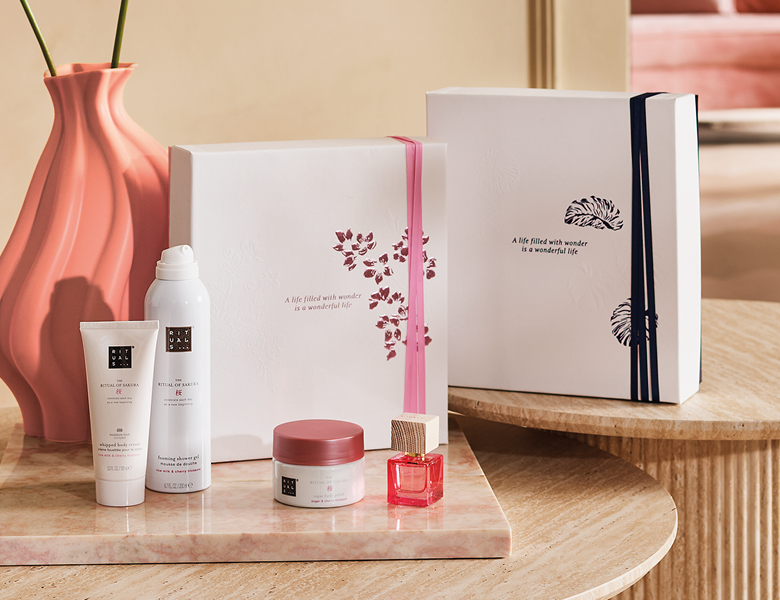 Her ses RITUALS gaveæsker og kropsplejeprodukter placeret på et bord i et lyst miljø.