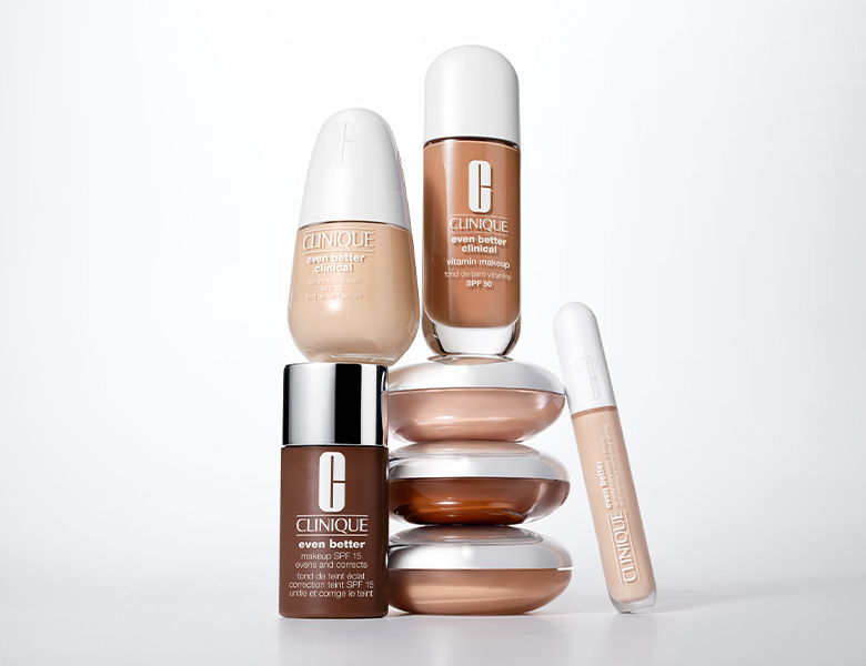 Her ses et billede med makeup-produkter fra Clinique placeret på dekorative glasformer mod en lys baggrund. Produkterne omfatter blandt andet foundation og concealer fra “Even Better”-serien.