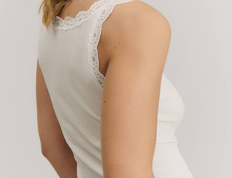 Her ses en kvindes torso bagfra. Hun har en hvid Rosemunde top på. 