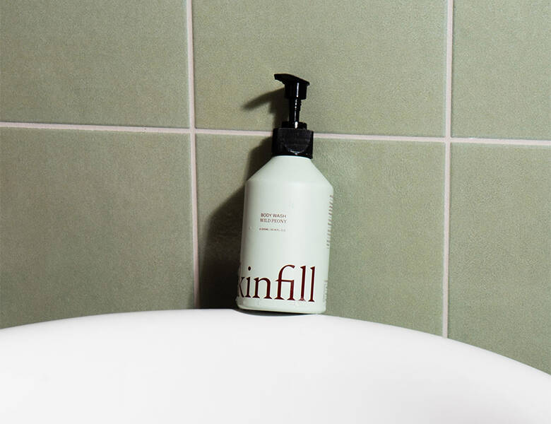 Her ses et Kinfill produkt, som står på kanten af et badekar op ad en grøn væg. 