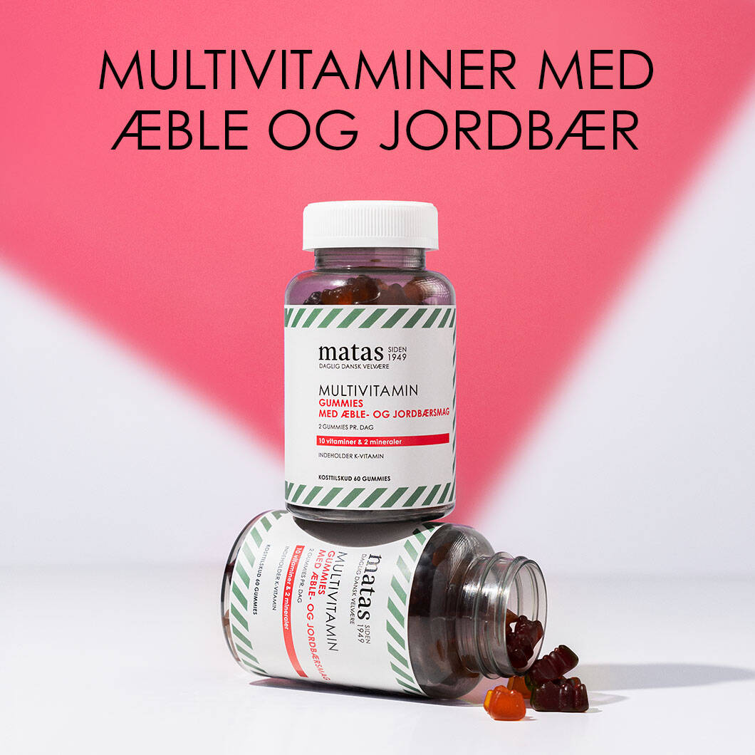 Her ses en rød og hvid baggrund med en sort tekst øverst. Under ses to bøtter af Matas vitaminvingummier med æble- og jordbærsmag. Den ene bøtte er liggende og åben, hvor der er nogle enkelte vingummier på vej ud. 