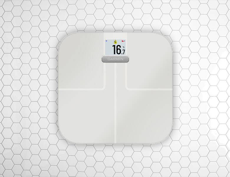 Hvid Garmin kropsvægt med digitalt display står på et gulv med hvide sekskantede fliser.