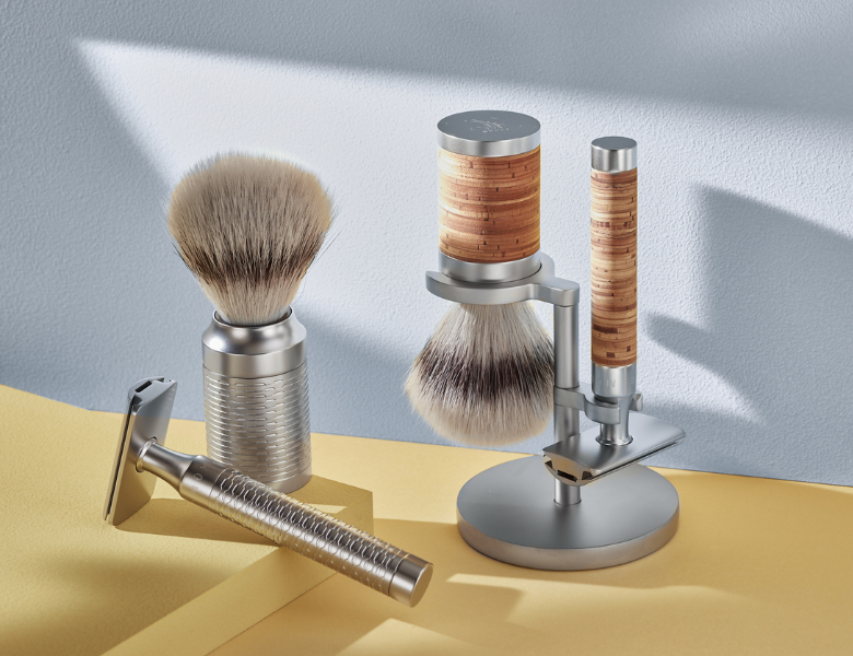 Mühle barbergrej står opstillet i blødt lys, herunder skraber, barberkost og holder med detaljer i metal og kork.
