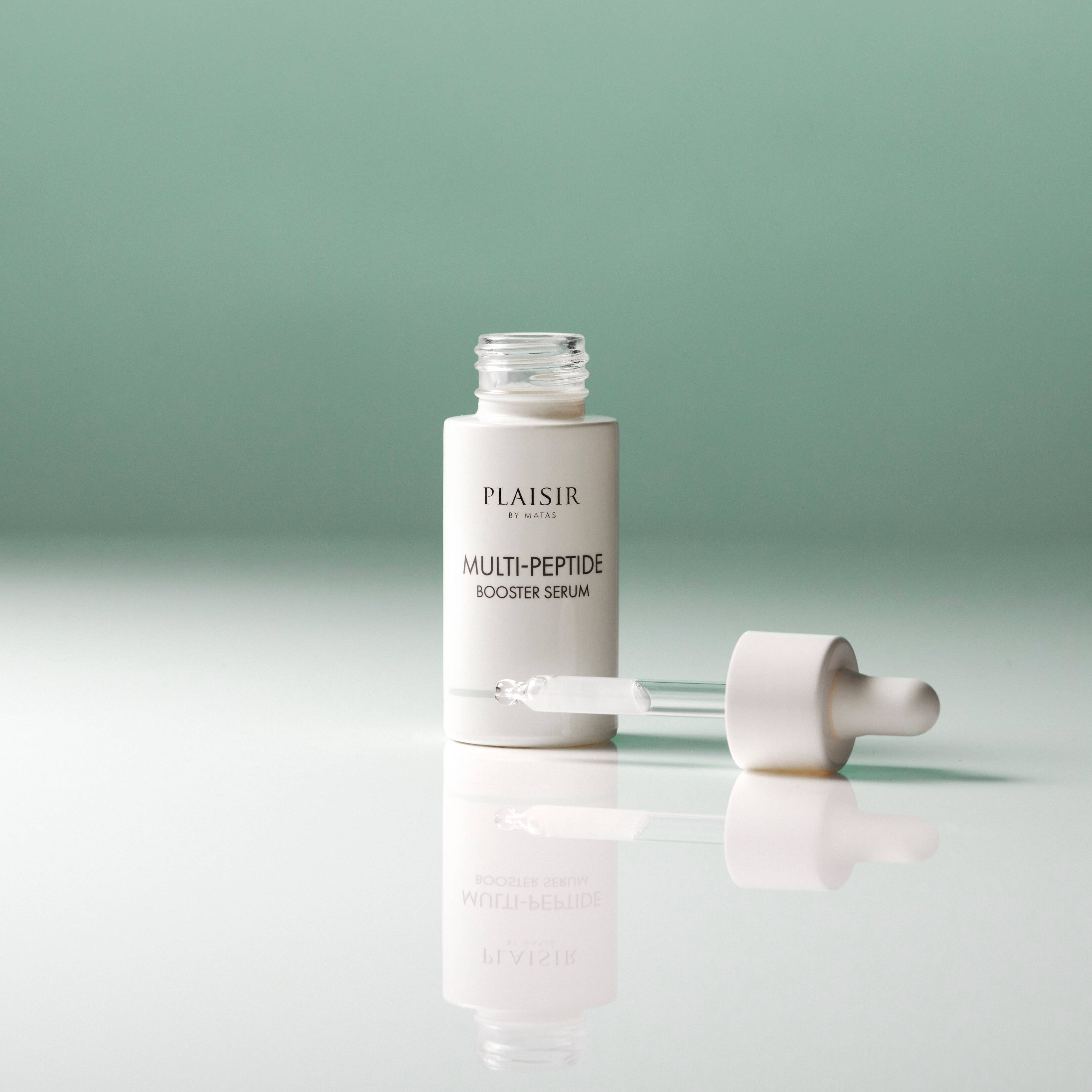 En flaske Plaisir Multi-Peptide Booster Serum står åben på en blank overflade mod en grøn baggrund. Pipetten ligger ved siden af med en dråbe serum i spidsen. Flasken spejler sig i underlaget.