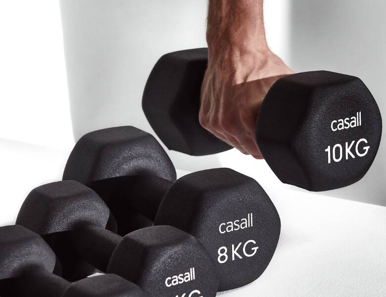 Her ses fire håndvægte i forskellige vægt KG. En mand tager den tungeste. Baggrunden er hvid. 