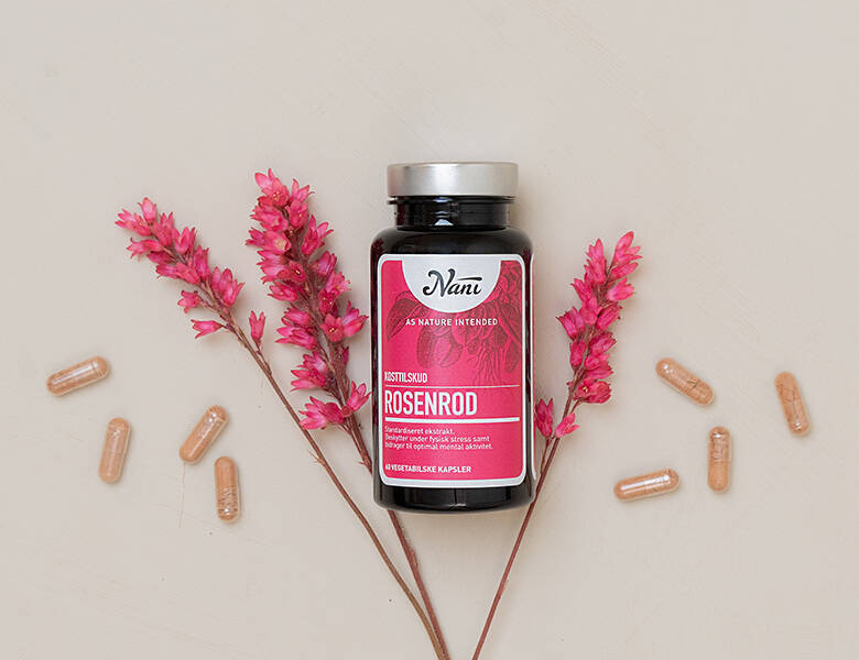 Her ses et lyserødt Nani produkt på en grå-beige baggrund. Rundt om produktet ses nogle lyserøde blomster samt nogle piller. 