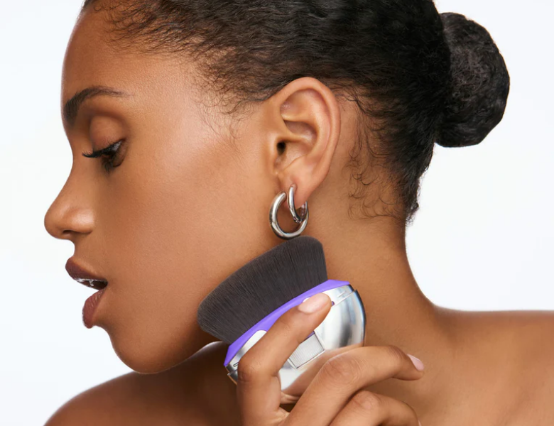 Her ses et nærbillede af en person, der anvender en stor makeupbørste fra Wonderskin på kæbelinjen. Personen ses i profil og holder børsten mod huden, hvilket viser produktets anvendelse til påføring eller blending af makeup.