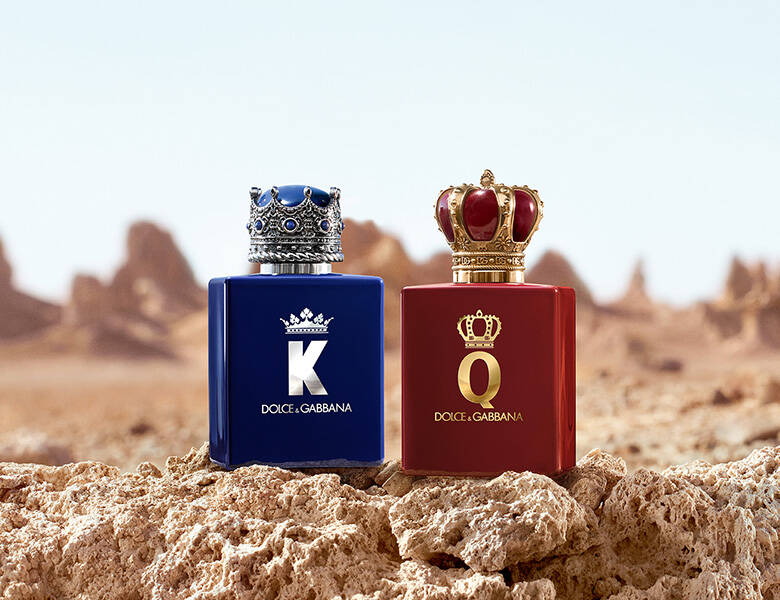 Dolce & Gabbana K og Q parfumer i blå og rød flaske med kronelåg står på klipper i et tørt ørkenlandskab